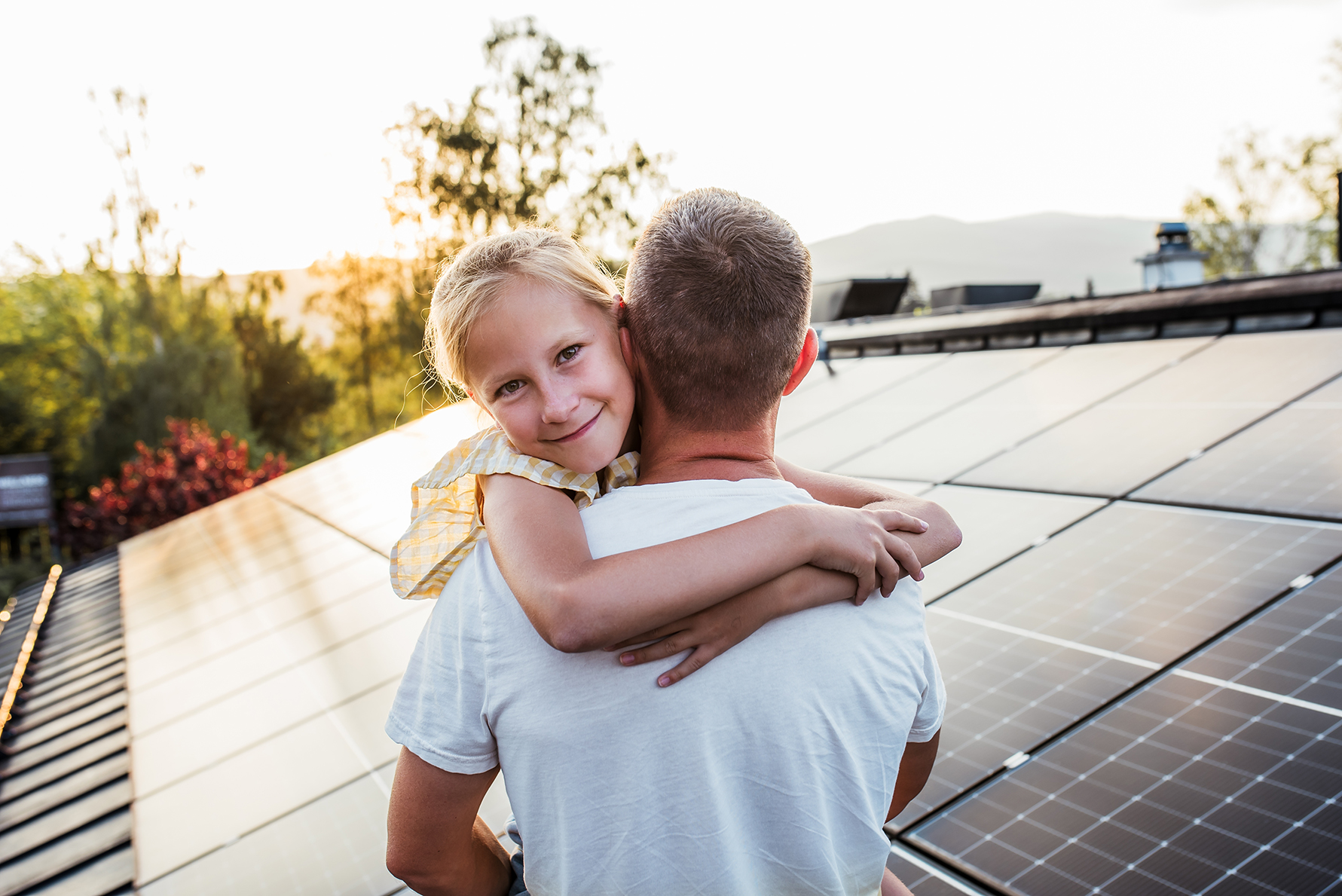 Smiling daughter hugging father on rooftop with solar panels.