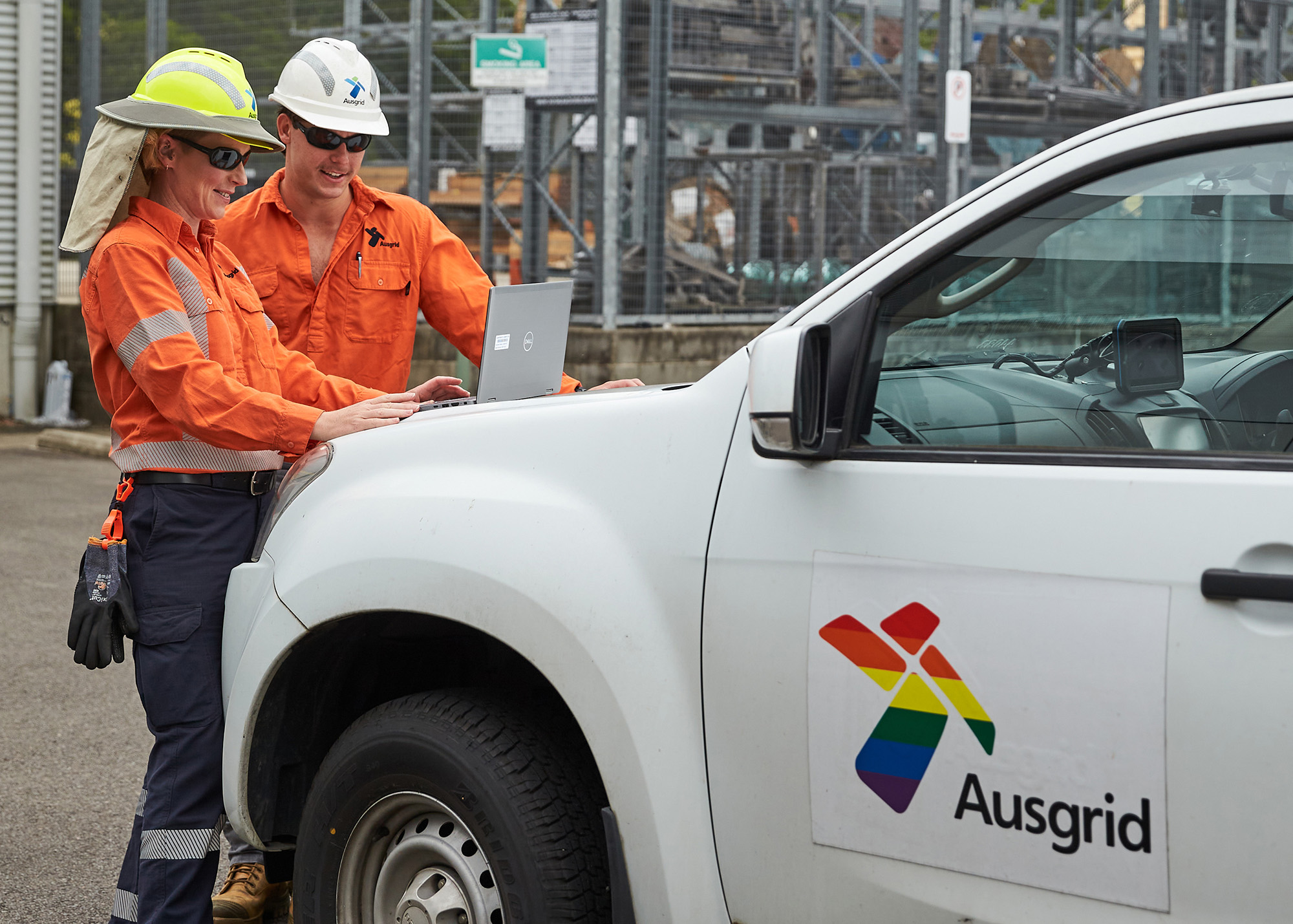 Two female employees in hats and Ausgrid crew uniforms checking an Ausgrid truck with Rainbow Ausgrid Logo