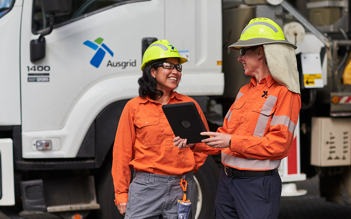 Two female field workers checking an ipad outdoors next to Ausgrid truck