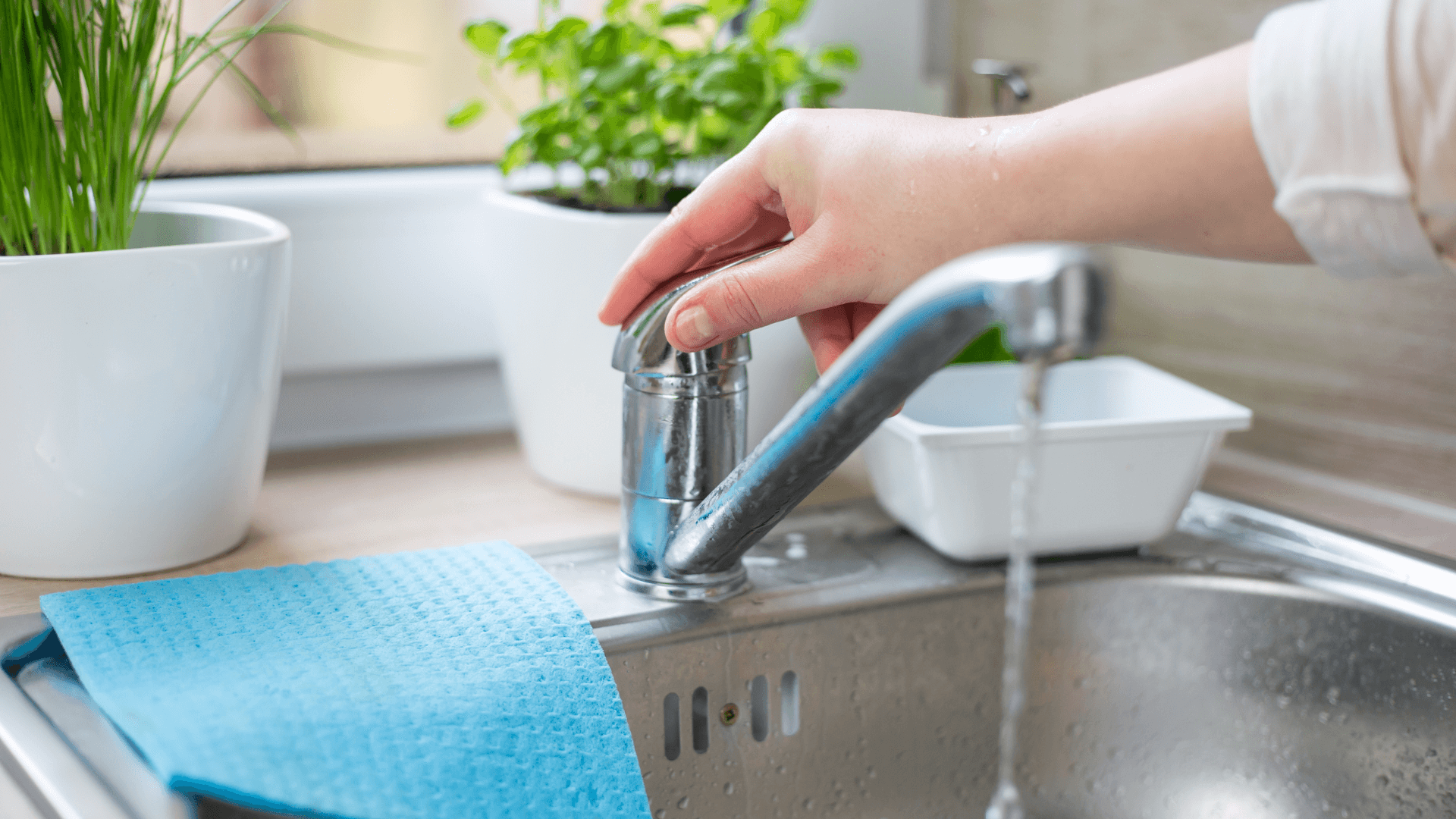 Person with hand on tap in kitchen with water running out of tap 